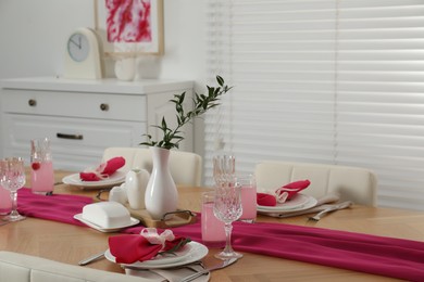 Photo of Color accent table setting. Glasses, plates, pink napkins and vase with green branch in dining room