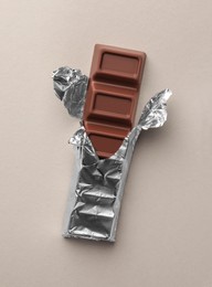 Photo of Tasty chocolate bar wrapped in foil on light background, top view