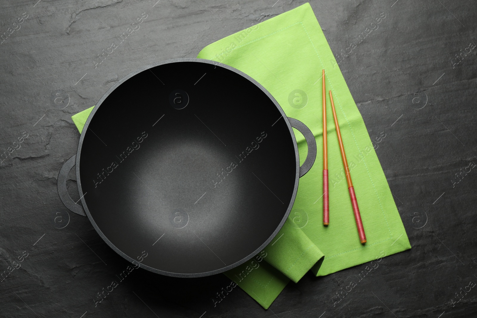 Photo of Empty iron wok and chopsticks on black slate table, top view