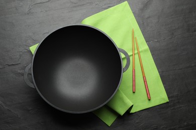 Photo of Empty iron wok and chopsticks on black slate table, top view