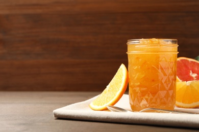 Photo of Delicious orange marmalade and fresh fruits on wooden table. Space for text