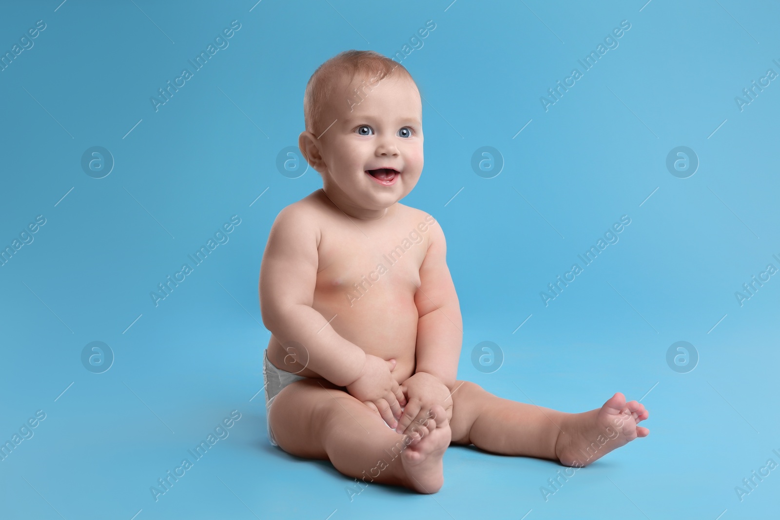 Photo of Cute baby in dry soft diaper sitting on light blue background