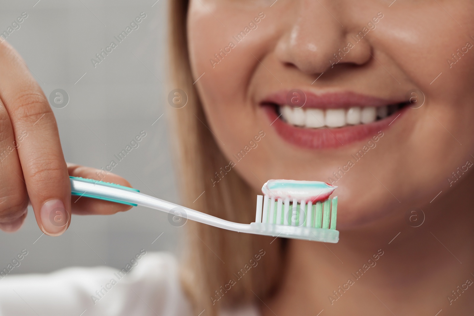 Photo of Woman holding brush with toothpaste in bathroom, closeup