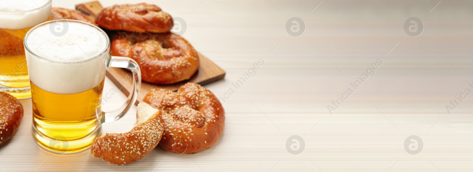 Image of Tasty pretzels and glasses of beer on white wooden table, space for text. Banner design