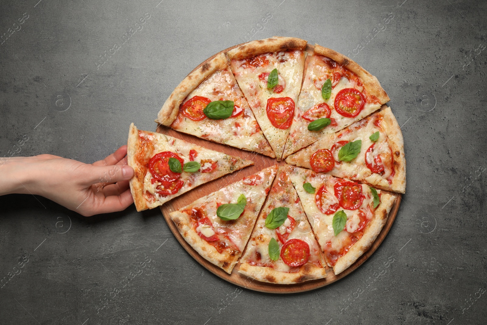 Photo of Woman taking slice of delicious pizza Margherita at grey table, closeup