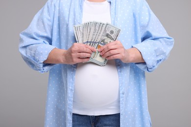 Photo of Surrogate mother. Pregnant woman with dollar banknotes on light grey background, closeup