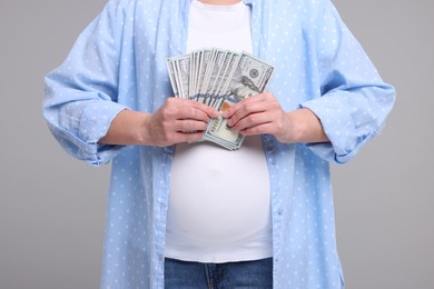 Surrogate mother. Pregnant woman with dollar banknotes on light grey background, closeup