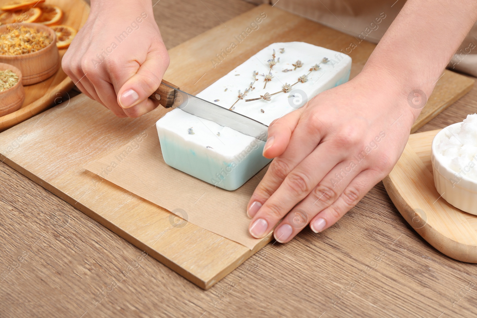 Photo of Woman cutting natural handmade soap on wooden table, closeup