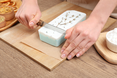 Woman cutting natural handmade soap on wooden table, closeup