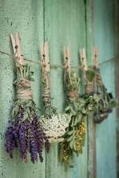 Photo of Bunches of different beautiful dried flowers hanging on rope near old wooden wall