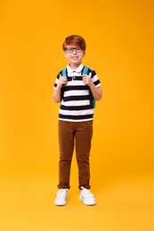 Happy schoolboy in glasses on orange background