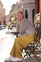 Beautiful senior woman sitting in outdoor cafe, space for text