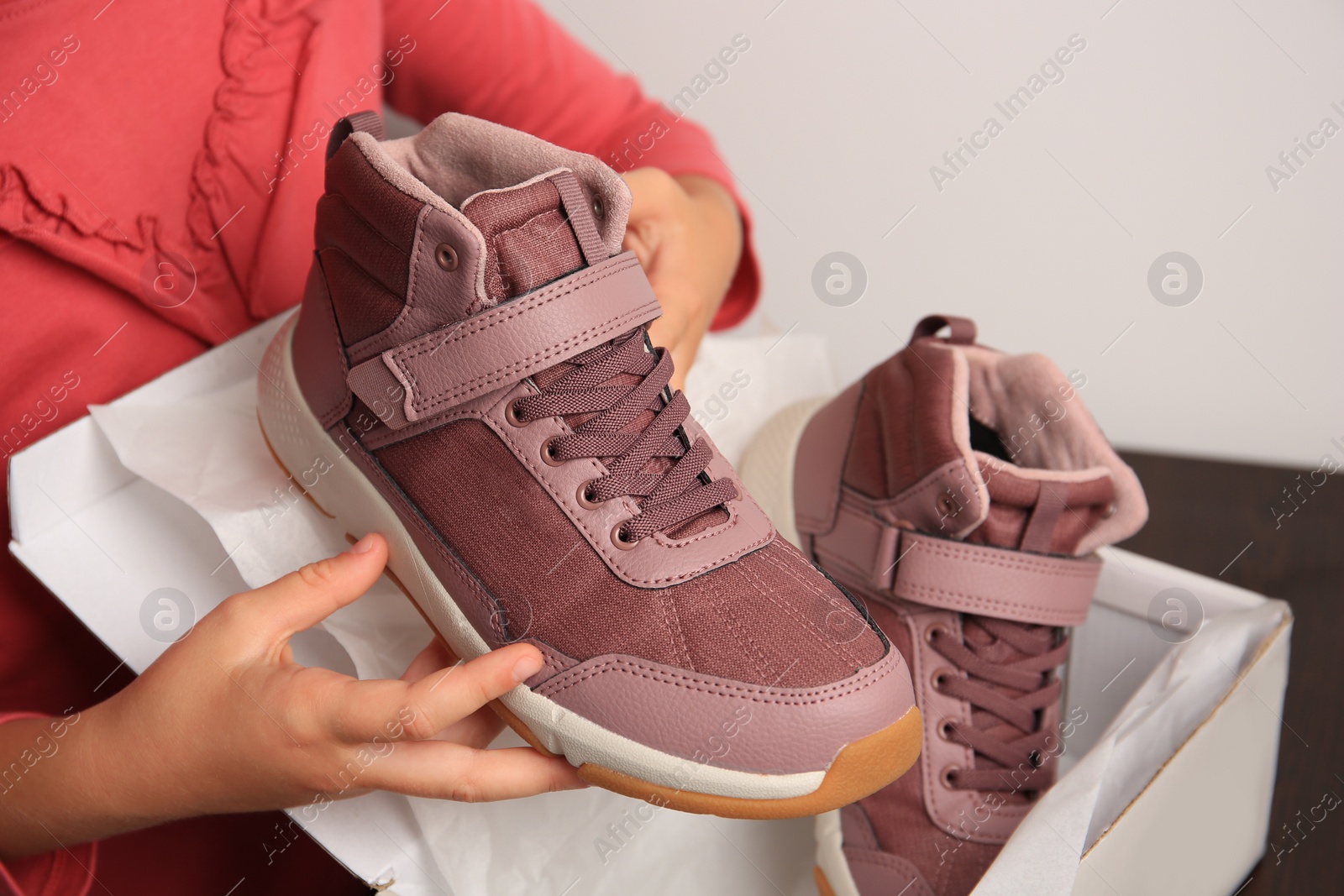 Photo of Girl taking out new sneakers from box at wooden table against light grey background, closeup