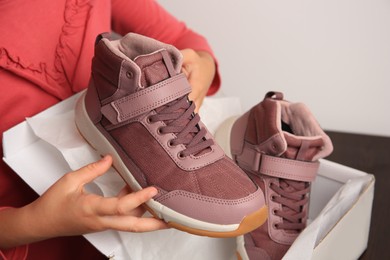 Photo of Girl taking out new sneakers from box at wooden table against light grey background, closeup