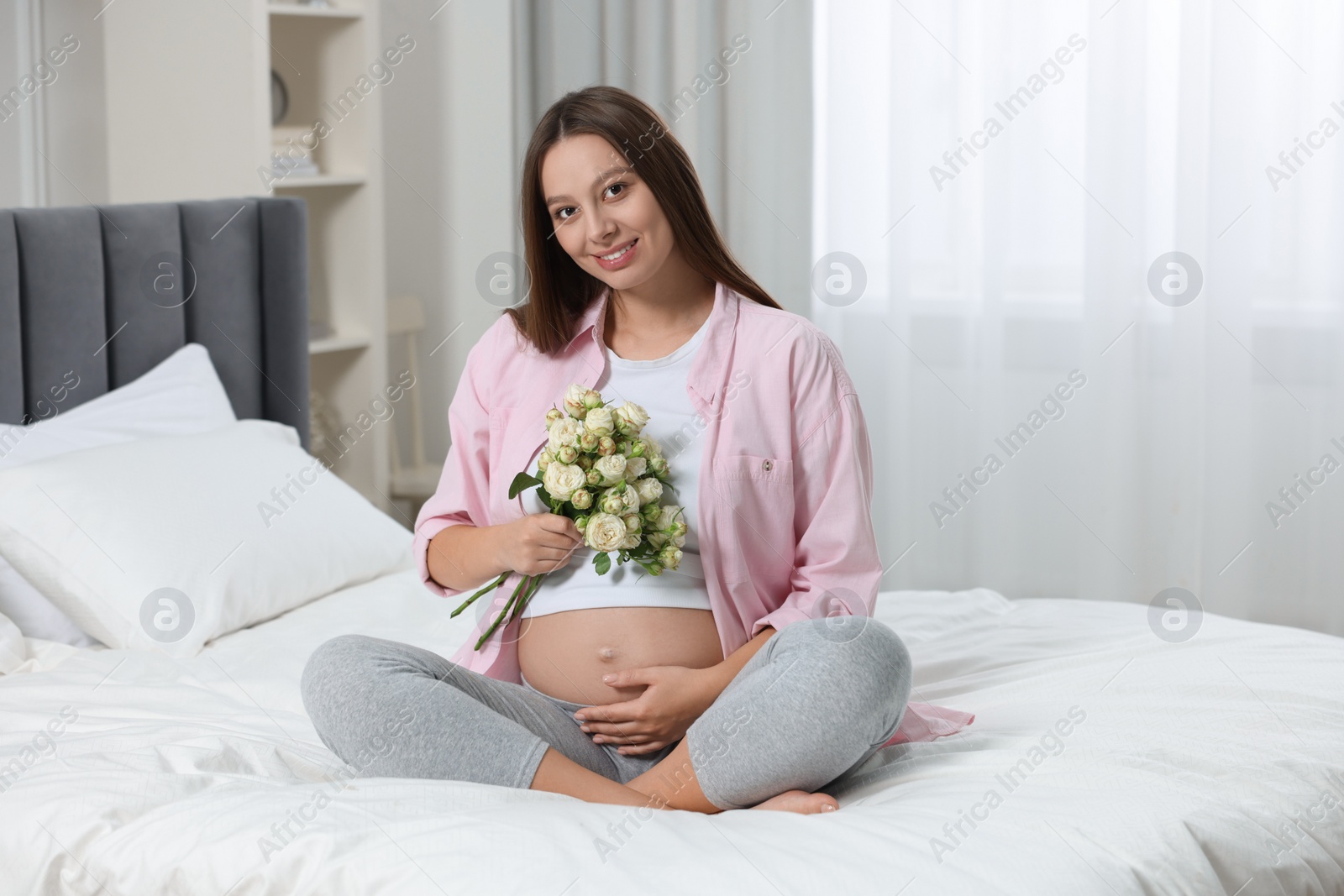 Photo of Beautiful pregnant woman with bouquet of roses in bedroom