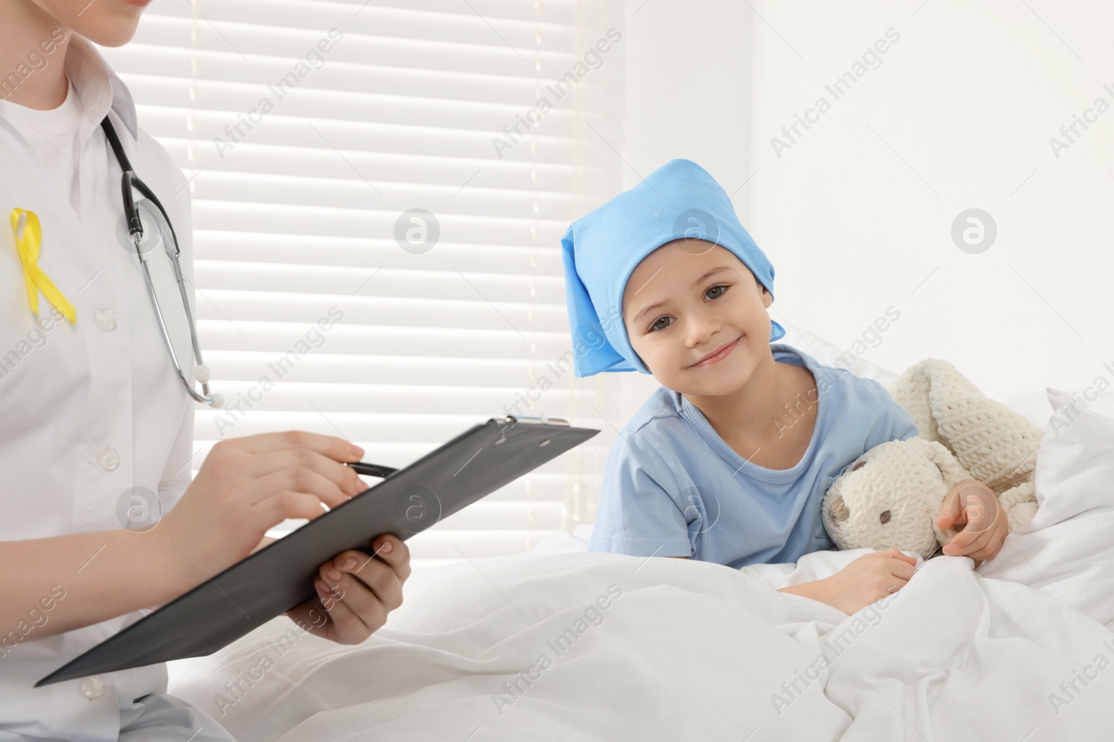 Photo of Childhood cancer. Doctor with clipboard and little patient with toy bunny in hospital