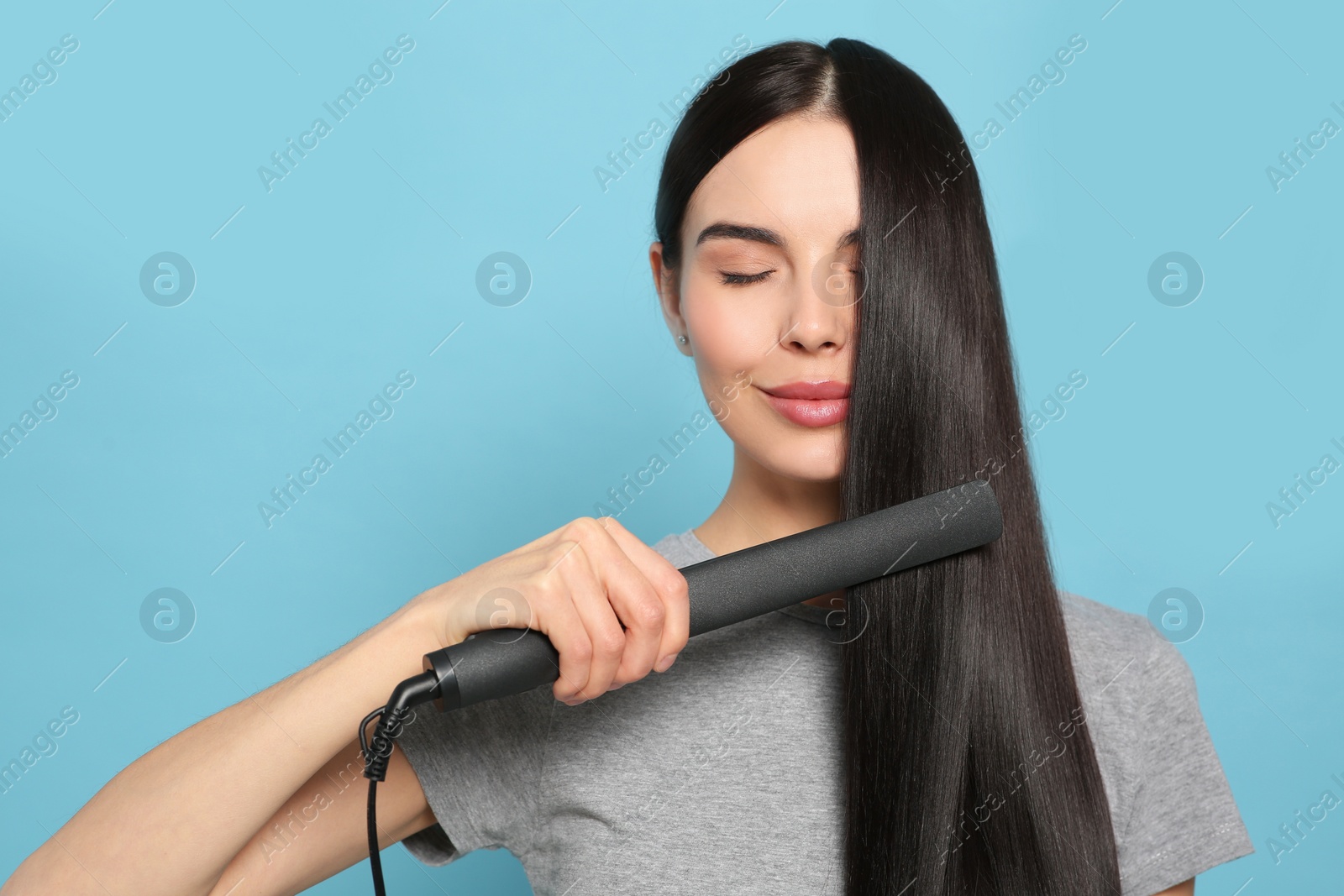 Photo of Beautiful woman using hair iron on light blue background