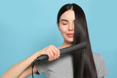 Beautiful woman using hair iron on light blue background