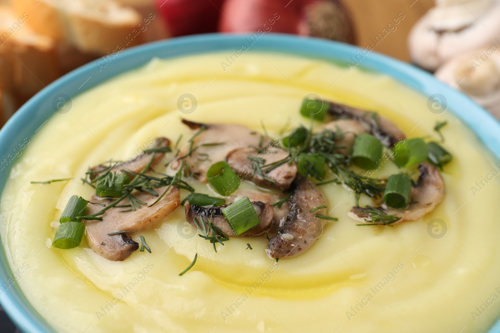 Photo of Bowl of tasty cream soup with mushrooms, green onions and dill on table, closeup