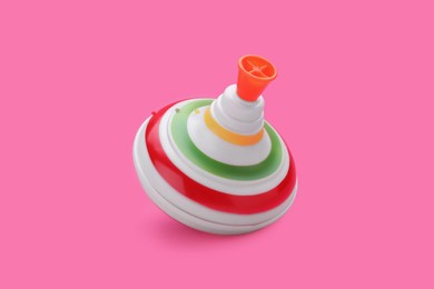 Photo of One bright spinning top on pink background, space for text. Toy whirligig