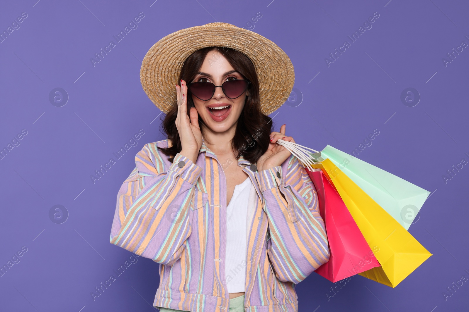 Photo of Beautiful young woman with paper shopping bags on purple background