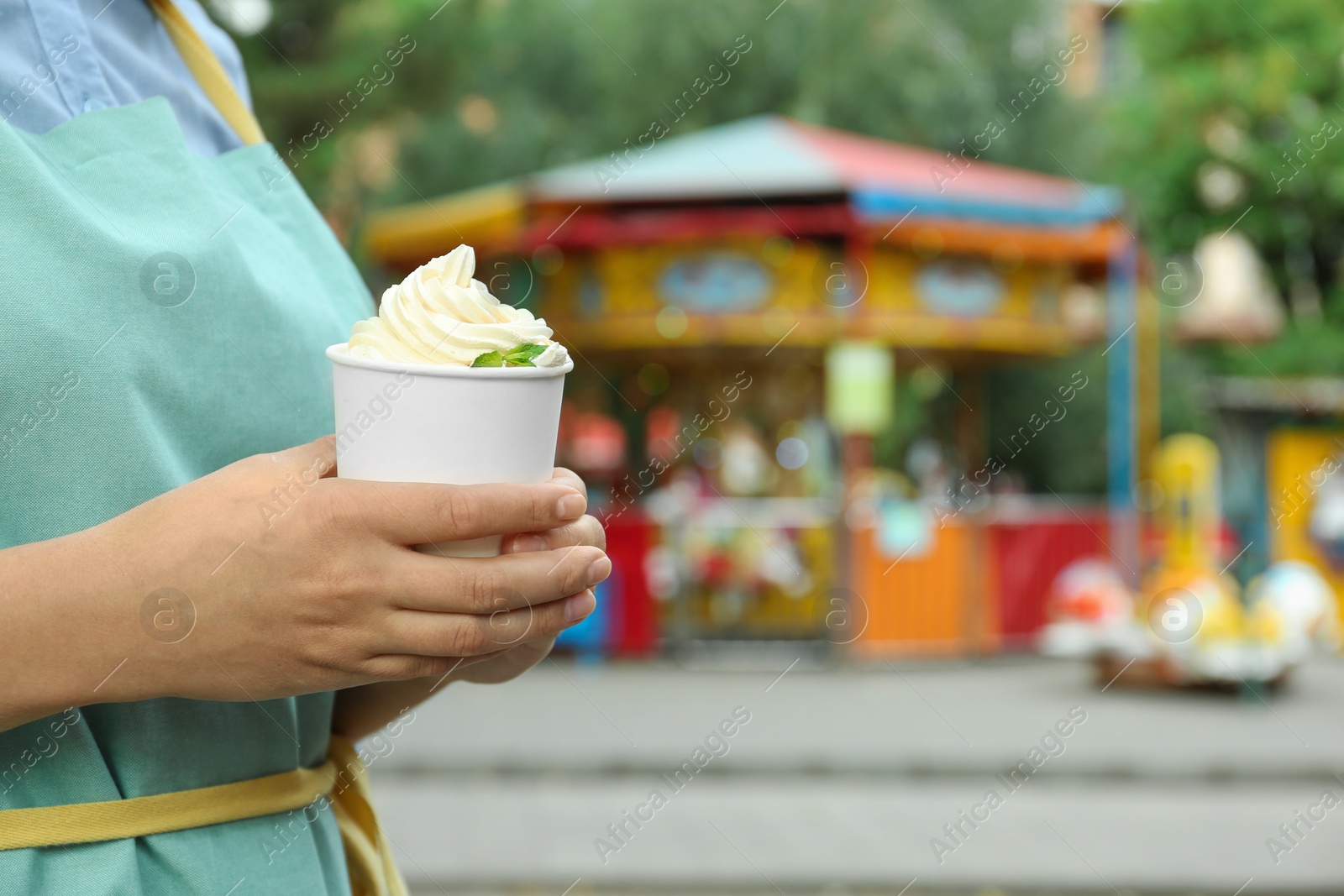 Photo of Woman holding cup with tasty frozen yogurt outdoors, closeup. Space for text