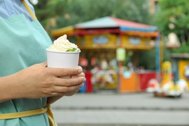 Woman holding cup with tasty frozen yogurt outdoors, closeup. Space for text