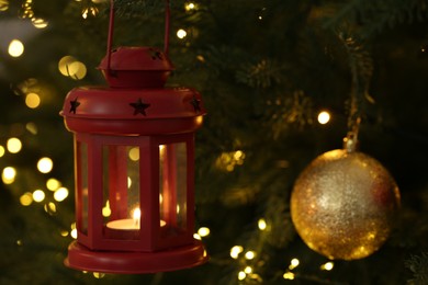 Photo of Christmas lantern with burning candle on fir tree as background, closeup. Space for text