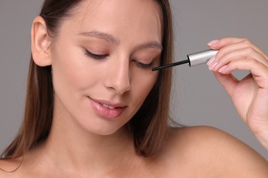 Photo of Beautiful woman applying serum onto eyelashes on grey background, closeup