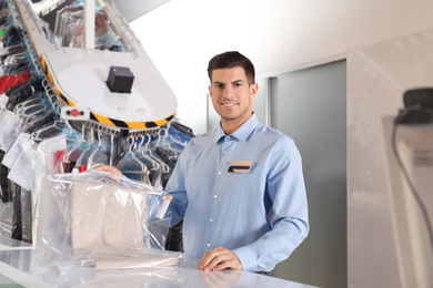 Portrait of happy worker with clothes near counter at dry-cleaner's