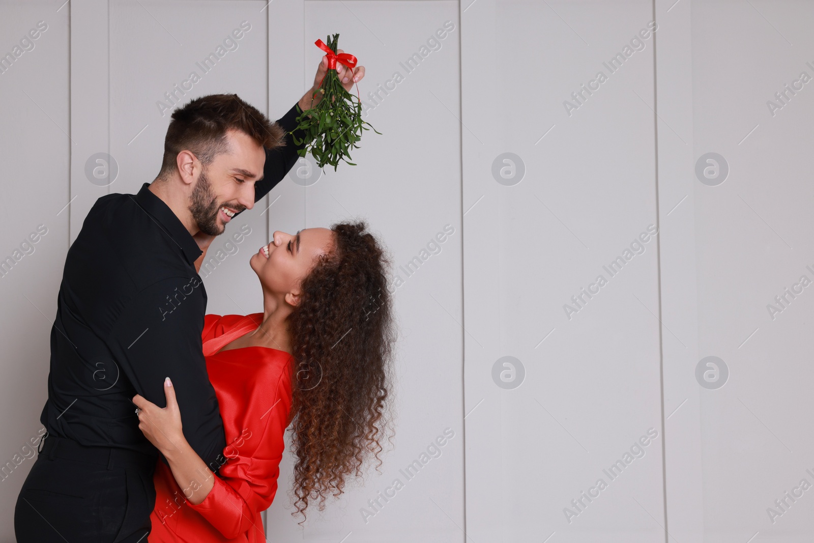 Photo of Lovely couple dancing under mistletoe bunch near light grey wall. Space for text