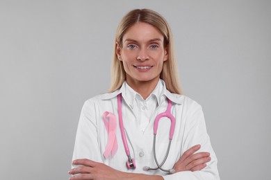 Doctor with pink ribbon and stethoscope on light grey background. Breast cancer awareness