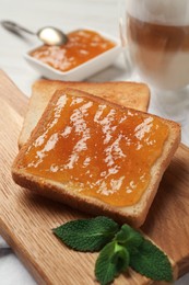 Photo of Toast with tasty orange jam, roasted slice of bread and mint on wooden board, closeup