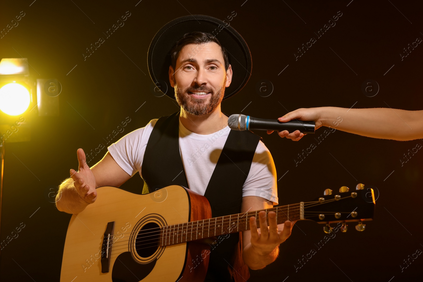 Photo of Handsome man with acoustic guitar singing while woman holding microphone on dark background, closeup