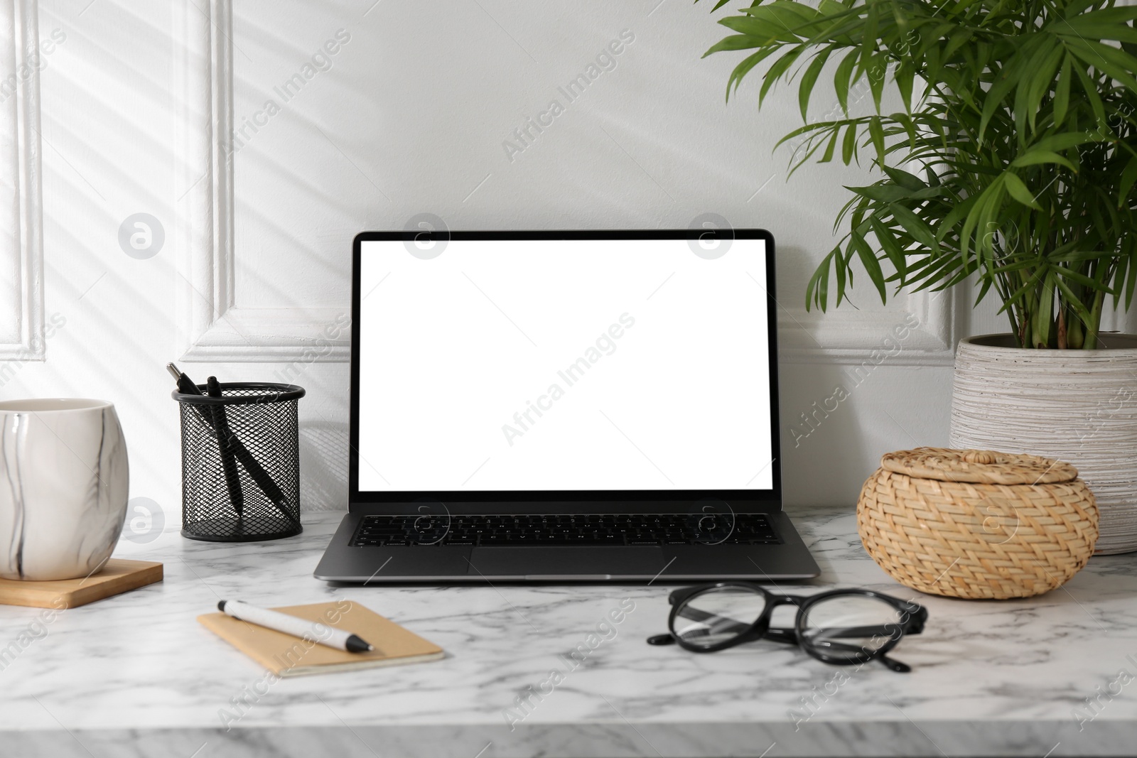 Photo of Office workplace with computer, glasses, cup and stationery on marble table near white wall