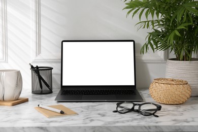 Office workplace with computer, glasses, cup and stationery on marble table near white wall