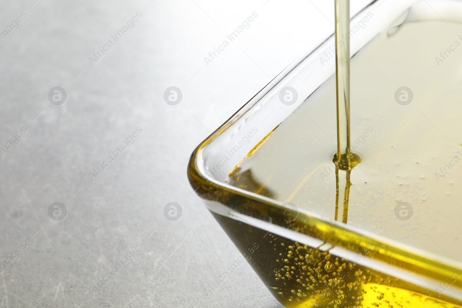 Photo of Pouring fresh olive oil into bowl on grey background, closeup