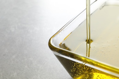 Pouring fresh olive oil into bowl on grey background, closeup