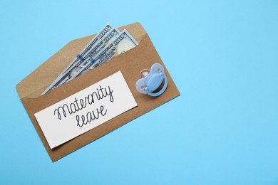Photo of Maternity leave concept. Envelope with dollar banknotes, pacifier and note on light blue background, top view. Space for text