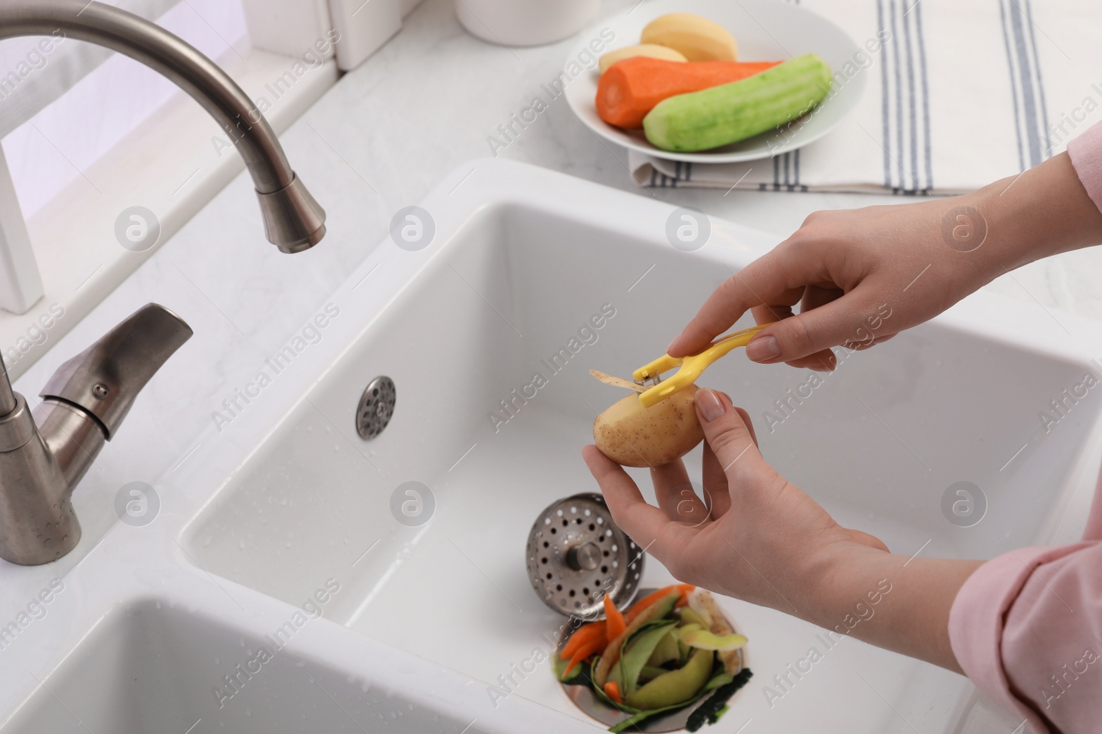 Photo of Woman peeling potato over kitchen sink with garbage disposal at home, closeup