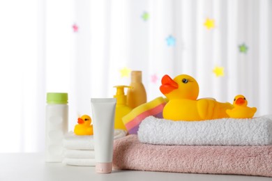 Towels, rubber ducks and baby care products on white table indoors