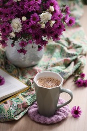Photo of Cup of aromatic coffee, beautiful flowers and bright cloth on wooden table