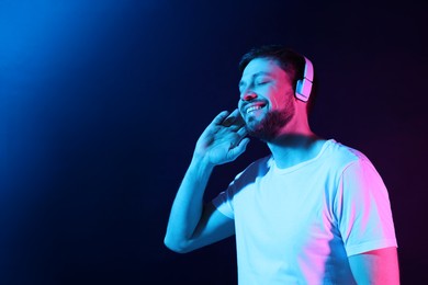 Photo of Happy man in headphones enjoying music in neon lights against dark blue background. Space for text