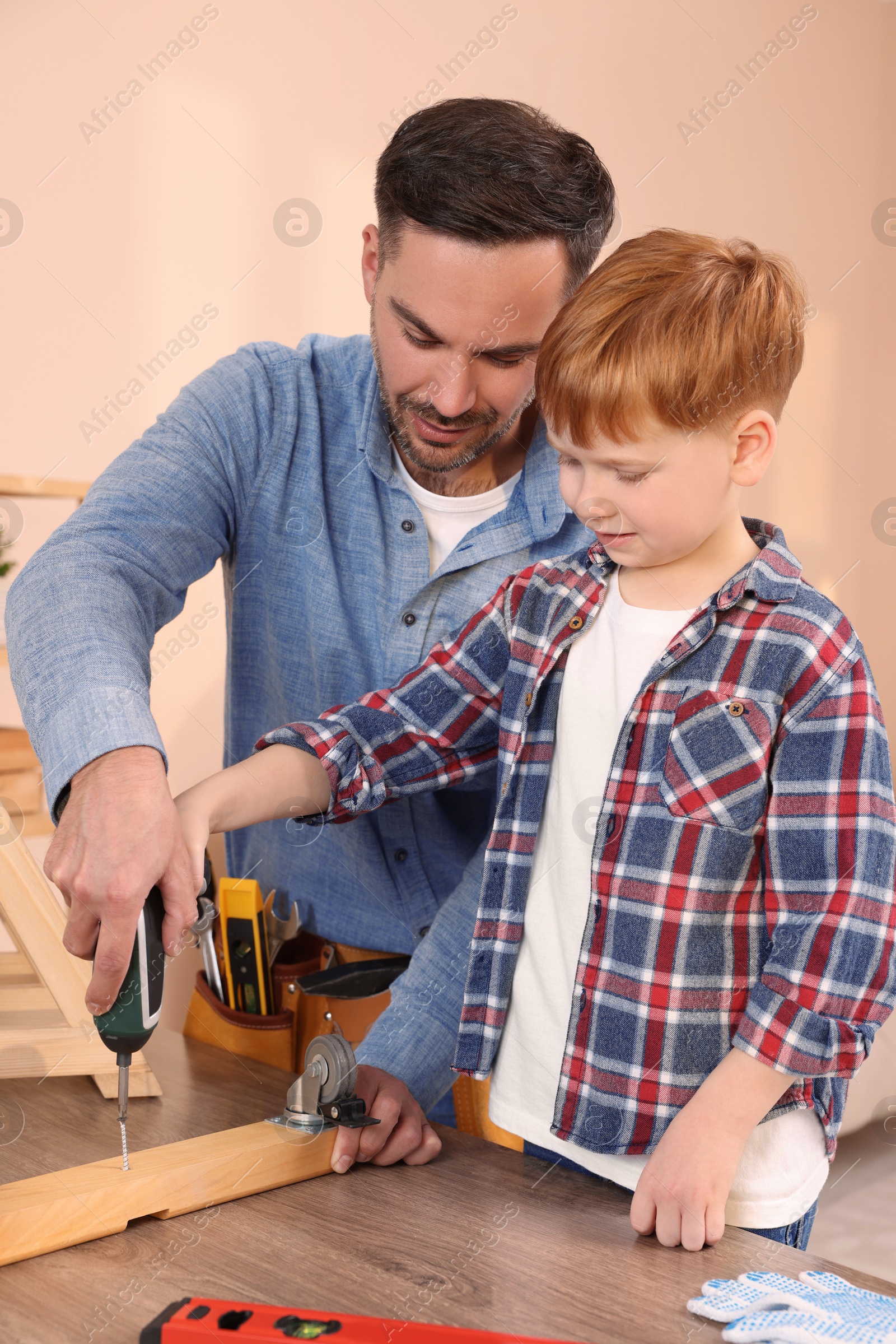 Photo of Father and son screwing wooden plank indoors. Repair work