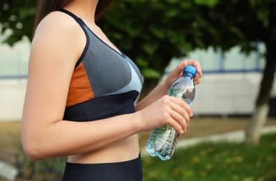 Sportswoman with bottle of water outdoors, closeup