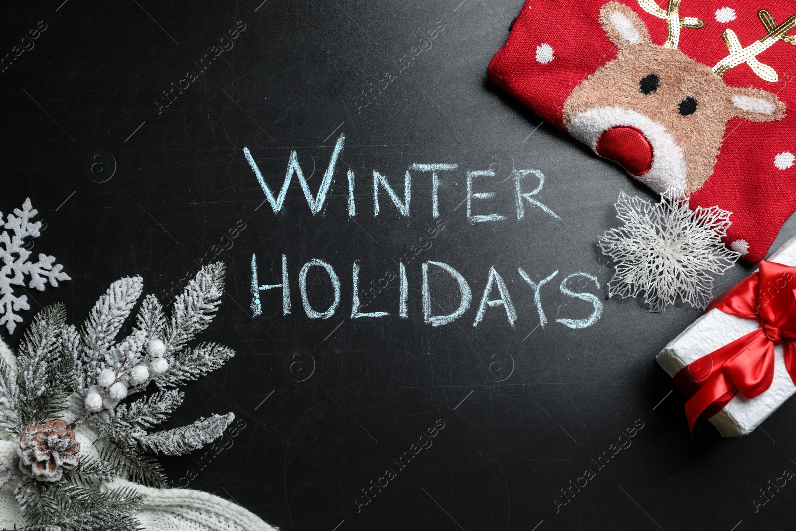 Photo of Flat lay composition of Christmas sweater, gift box and decorations on school blackboard with phrase Winter Holidays