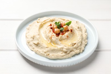 Photo of Tasty hummus with garnish on white wooden table