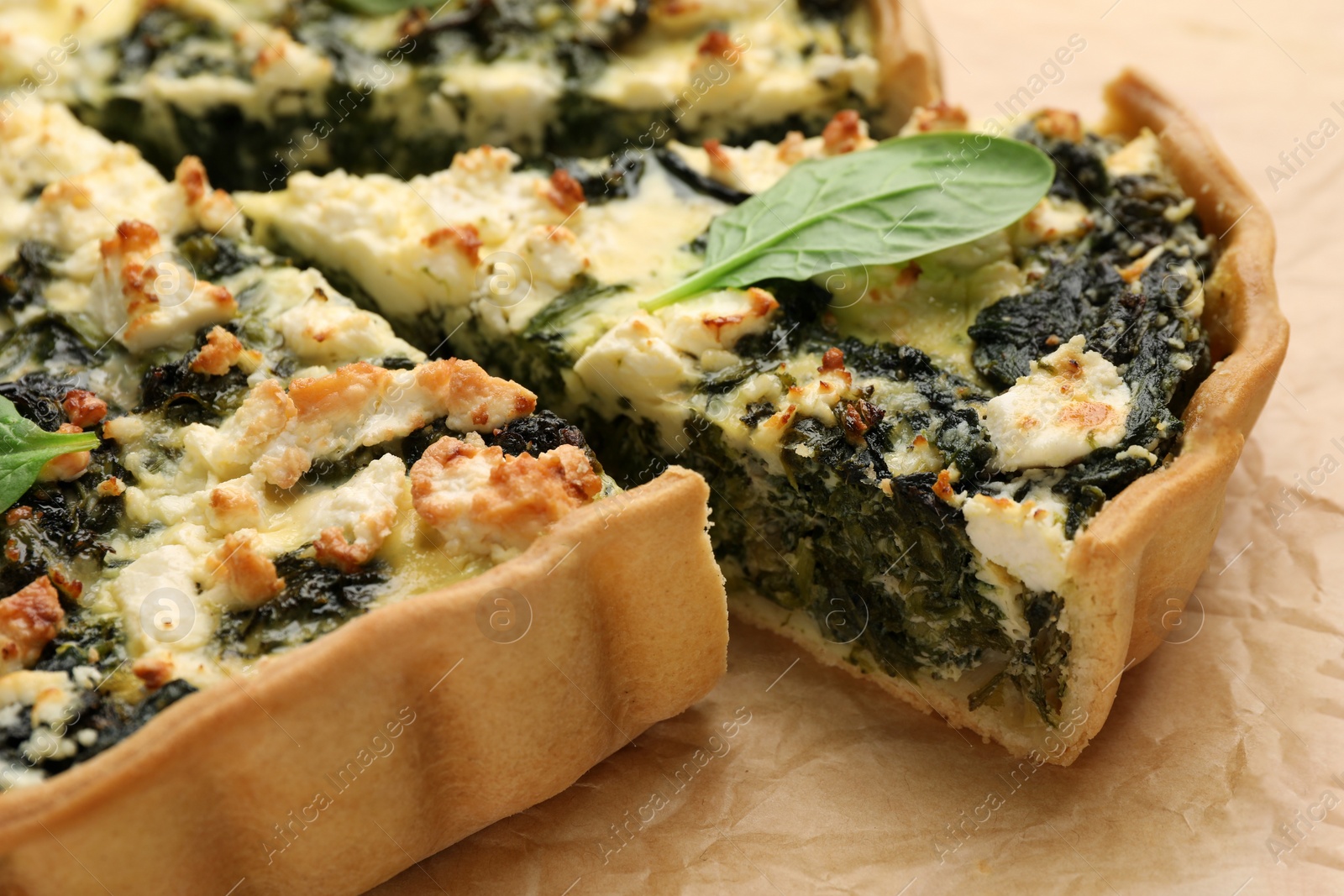 Photo of Delicious homemade spinach quiche on parchment paper, closeup