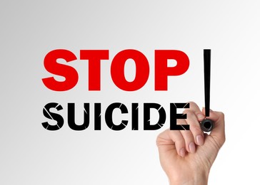 Woman writing phrase Stop Suicide on glass board against white background, closeup