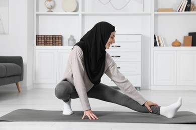 Photo of Muslim woman in hijab stretching on fitness mat at home